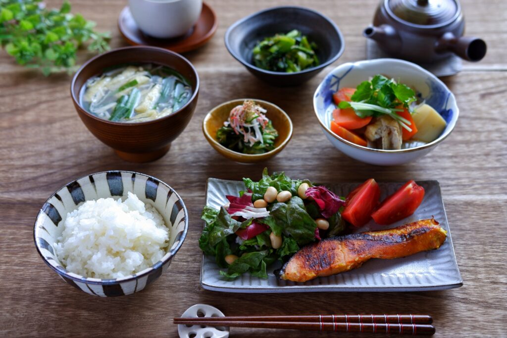 Image of a traditional Japanese meal, small portions with fish, rice, and different vegetables.
